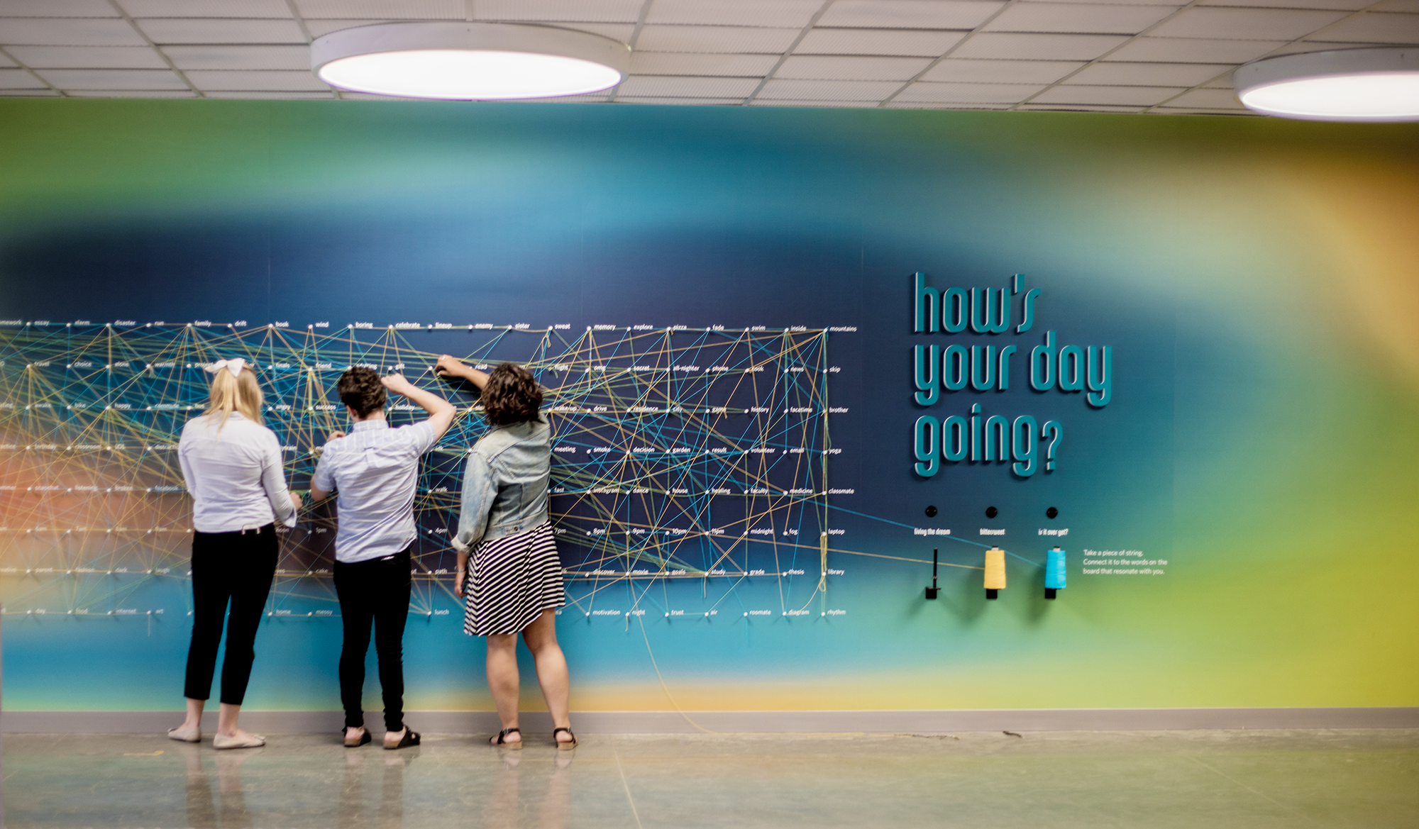 3 students interacting with the "hows your day going" wall at the ubc life building