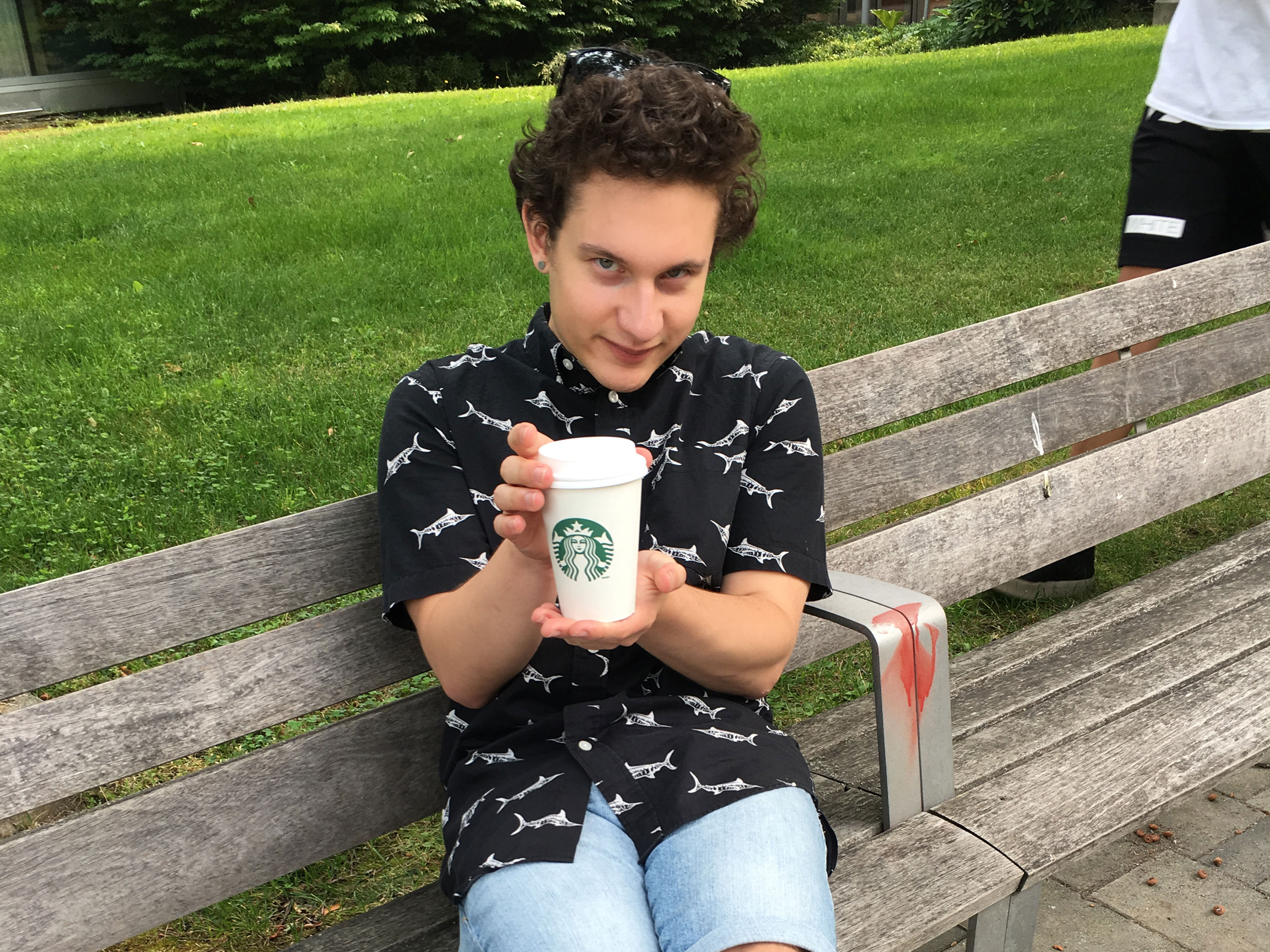 derrick holding a latte and sitting on a bench
