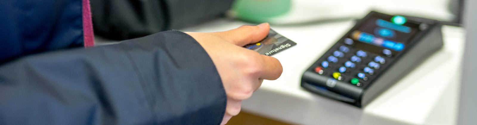 A student holding their credit card above a payment terminal