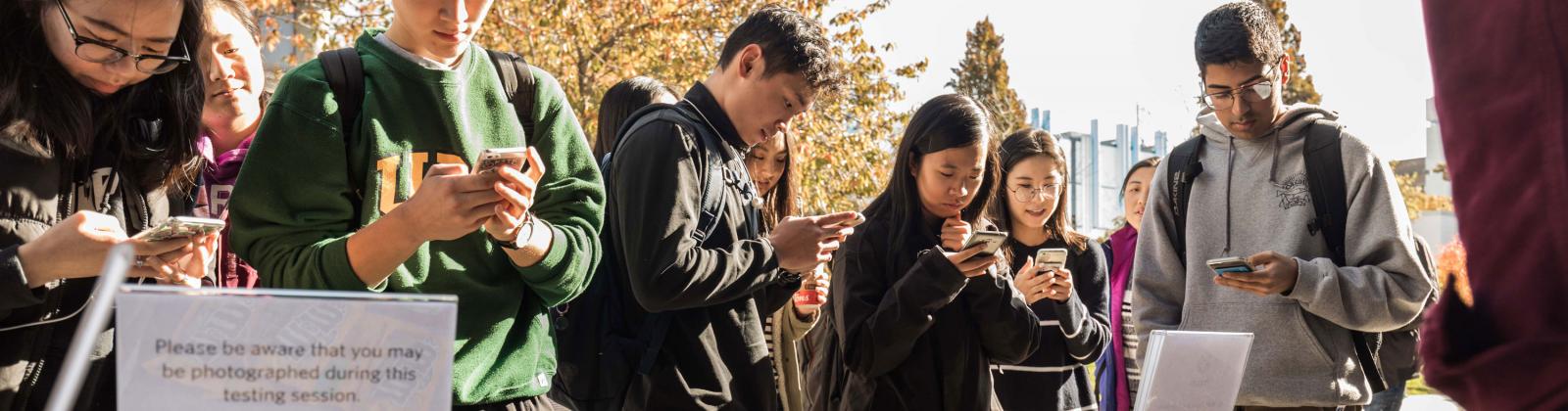 A group of students standing outdoors on their phones participating in UX research