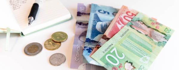 Bills and change on a desk alongside an expense notebook