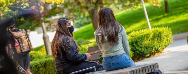 Two students sitting on a bench on campus
