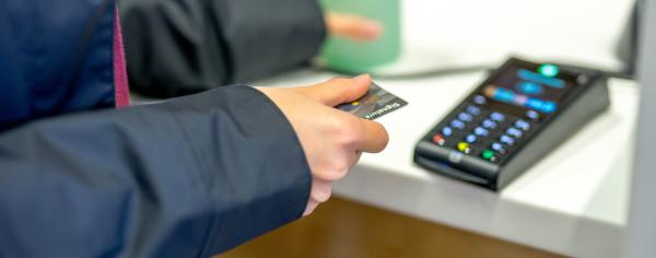 A student holding their credit card above a payment terminal