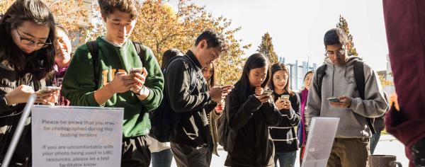A group of students standing outdoors on their phones participating in UX research