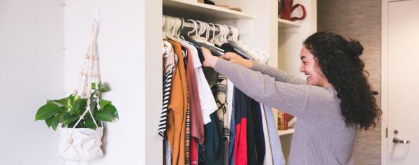 Student smiling while rummaging through a closet full of clothes.