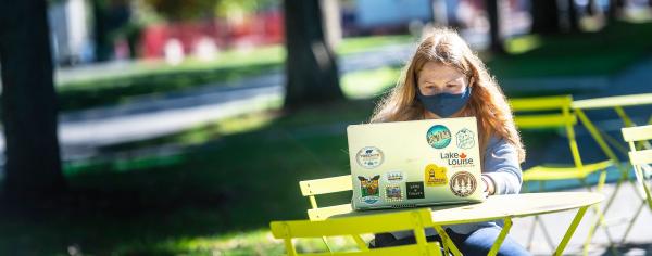 Student sitting outdoors at a picnic table looking at their computer