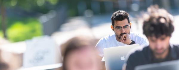 Student sitting outdoors staring quizzically at their laptop