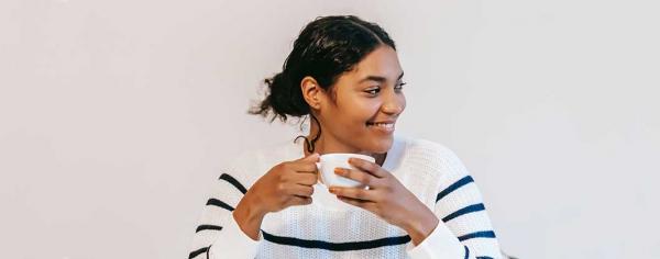 Student sitting in front of a blank wall smiling while holding a warm beverage