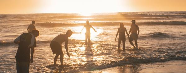 Group of friends standing in the ocean together at sunset