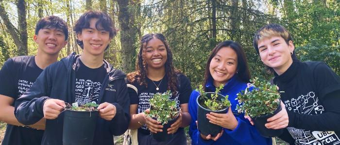 Five UBC students from the Climate Action Mobilizers team hold plants while posing for the photo