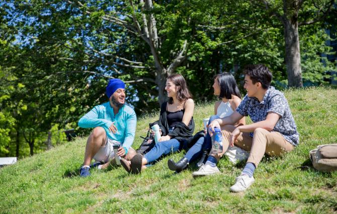 A group of students sitting outdoors on a hill talking and laughing together