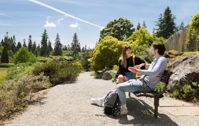 Two students sitting outdoors on a bench engaging in deep conversation