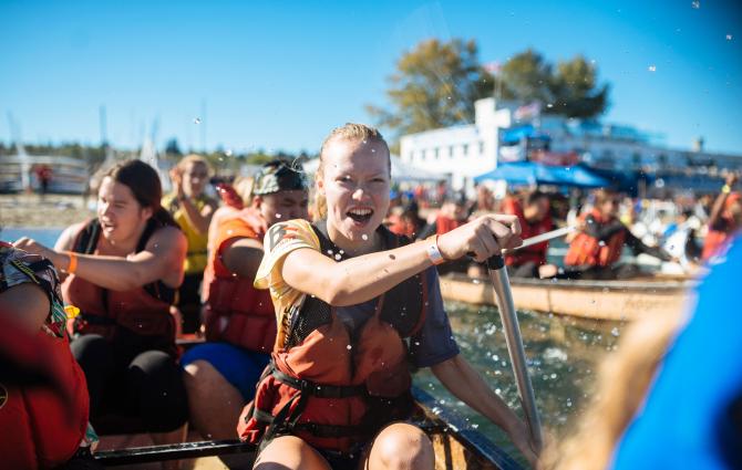 A student laughing while rowing in a longboat during UBC Day of the Longboat