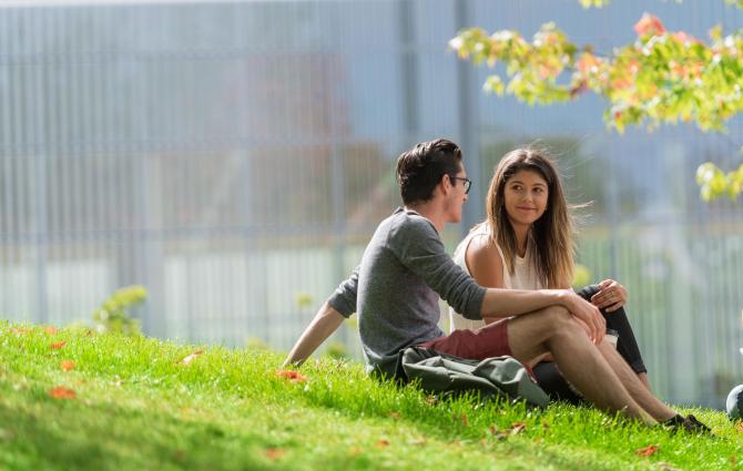Two students sitting together on a grassy hill engaging in a conversation