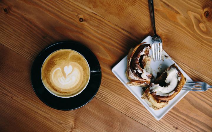 A coffee and cinnamon roll on a wooden table.