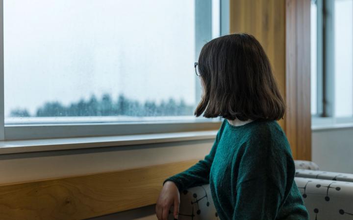A student is sitting by a window, looking out to the distance to a rainy and cloudy view.