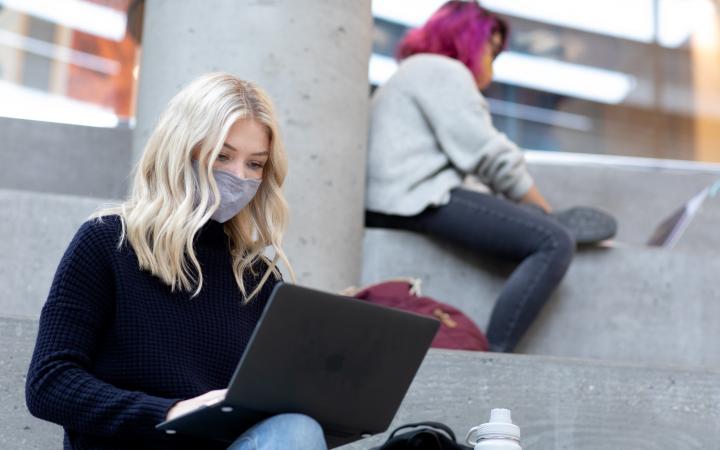 Student on laptop and wearing mask, studying indoors