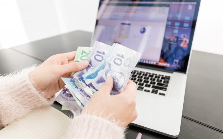 A student fanning out Canadian dollar bills in front of their laptop