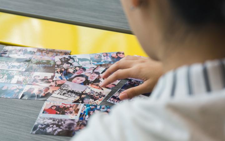 A student looking down at physical photos of her and her friends scattered on a desk