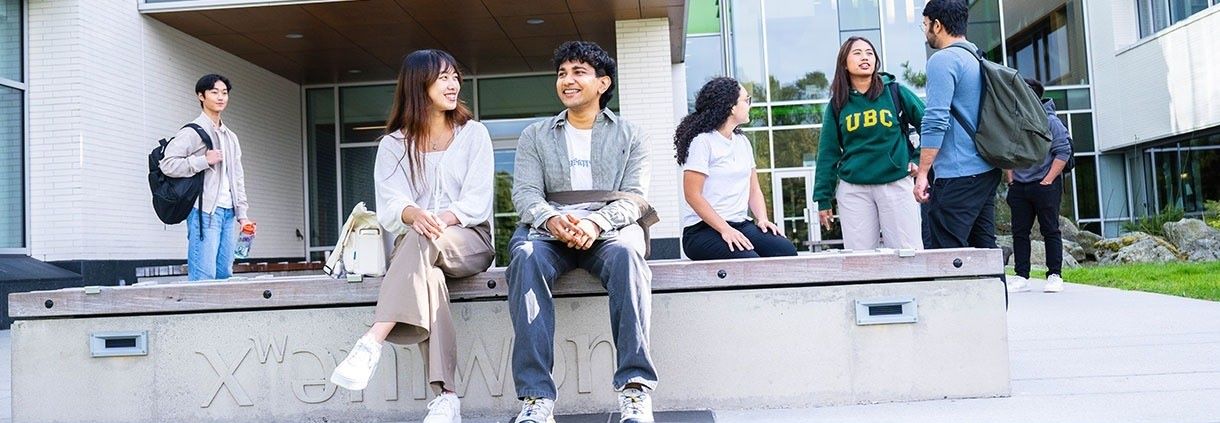 A group of UBC international students sit outside of a campus building at UBC Vancouver